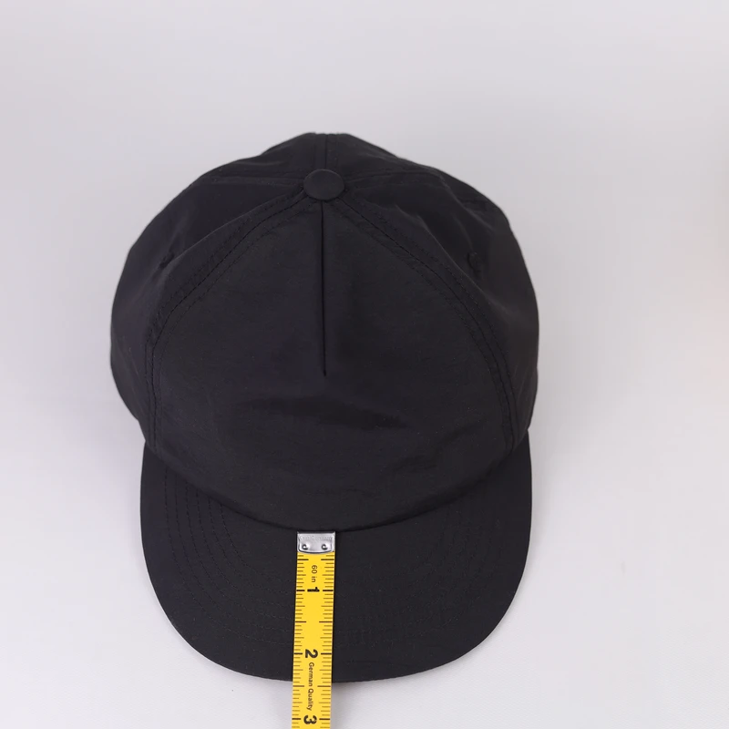 Tape measure checking visor length on a black short-brim baseball cap