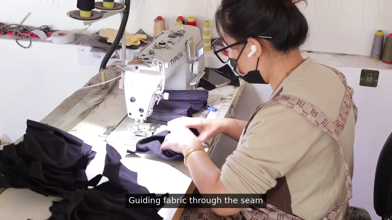 Operator guiding shaped fabric pieces through a sewing machine in the OEM Caps workshop